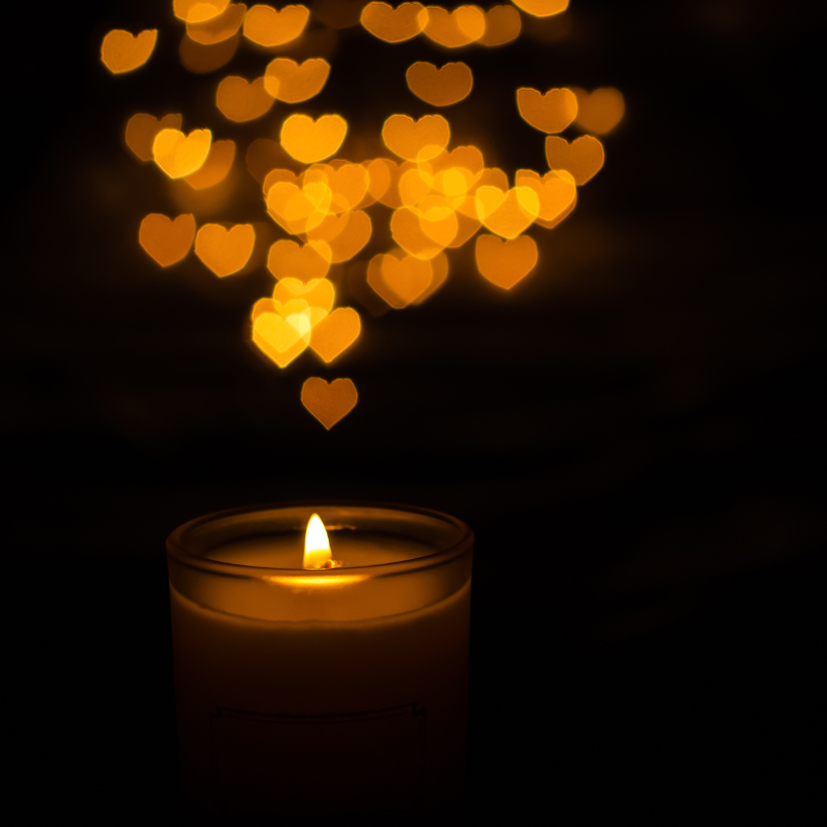 A glowing candle in the dark, with golden heart-shaped light rising gently above it — symbolizing the quiet beginnings of awakening.